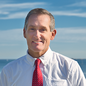 A man in a white shirt and a red tie smiles at the camera.