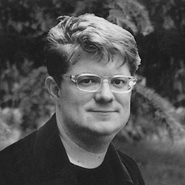 A person wearing glasses and posing in front of a tree.