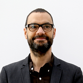 A person with glasses and a beard wearing a button down shirt.
