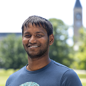 A person with sparse facial hair smiling, clock tower in background