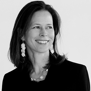 Black and white headshot of woman with earrings and hair down to her shoulders smiling.