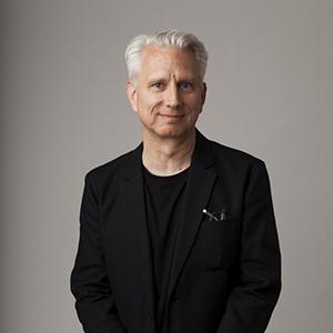 a man in a black shirt and jacket with white hair looking to camera