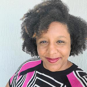 smiling woman with a striped pink and black shirt against a light blue backdrop