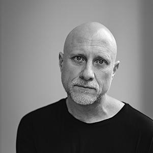 A bald man with light skin and a beard, wearing a black shirt.