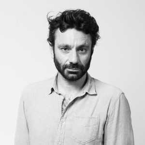 Black and white portrait of a person with brown hair and a beard, wearing a shirt