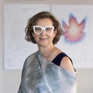 A fair-skinned woman with medium wavy blonde hair and wearing glasses with thick white frames looking at the camera.
