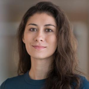 A fair-skined women wearing a navy-blue t-shirt ong brown hair falling over her left should facing the camera.