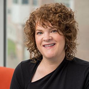 Woman with light brown curley hair smiling with a black shirt on. 