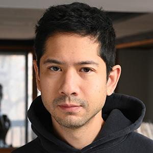 A man with short dark hair and stubble, wearing a black hoodie