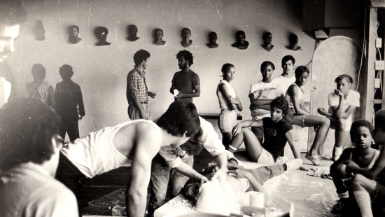 People standing around and sitting with artistic heads on the wall.