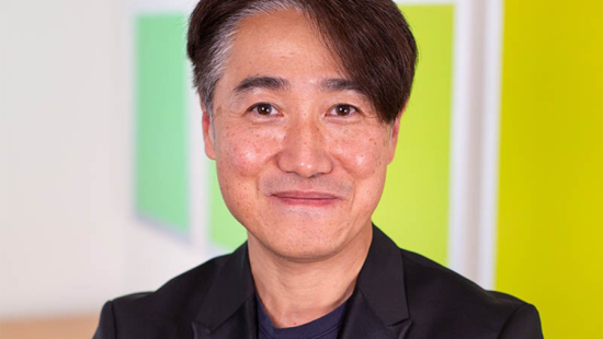 Asian man wearing dark suit jacket seated in front of brightly colored paintings