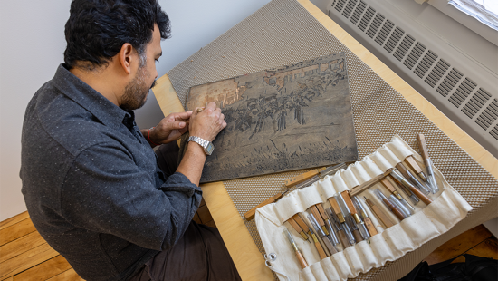 Seated man at work on a wood carving.
