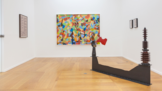 A white walled gallery with light wood floor and different sculptures and paintings on the wall