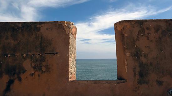 A thick stone balustrade overlooks a body of water beneath blue sky and clouds.