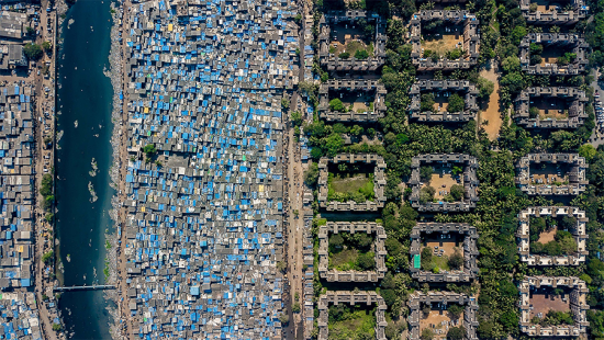 rows of sheet metal housing with blue roofs and large luxury concrete buildings next to them