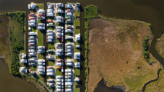 Aerial view of sunny house roofs surrounded by water and grassland.