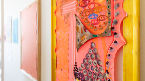 Bright pink material stretched across a yellow frame and illustrated with drawn eyes, circles, and lines.