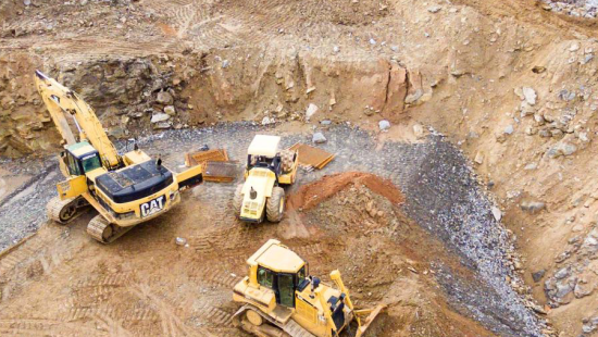 Heavy machinery and construction vehicles digging in a dirt pit.
