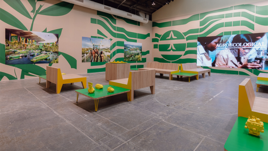 Fictional waiting lounge featuring bright green tables, yellow sculptures, and hung travel posters