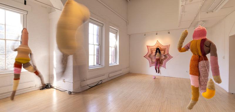 Four multicolored fabric humanoid figures hanging from a ceiling.