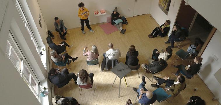 Group of people gathered around looking at a person presenting artwork.