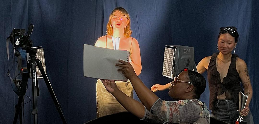 Three people in front of a dark blue curtain with a camera and production equipment.