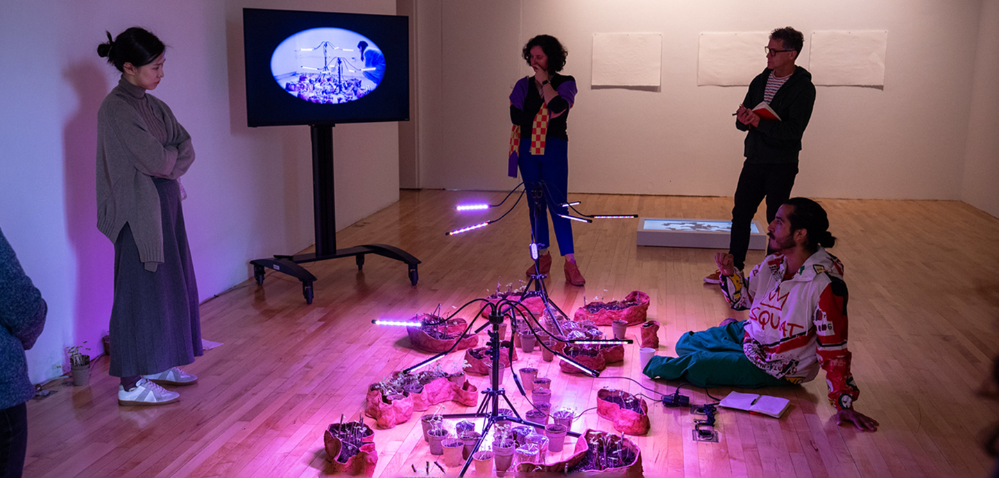 Four people reviewing a sculpture lit by purple light laying on the floor.