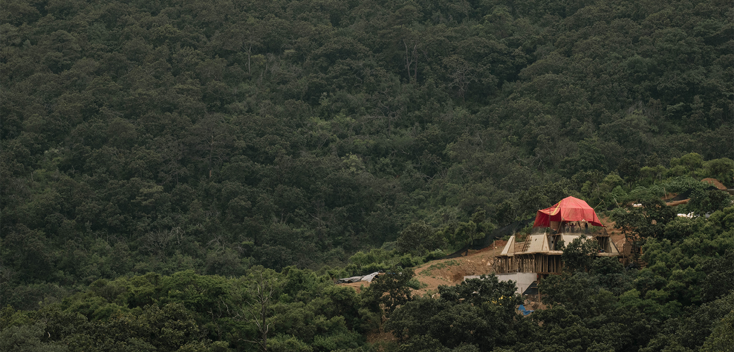 A red tent perched atop a grassy hill, surrounded by a clear blue sky and distant landscape.