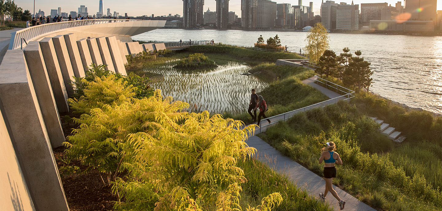 a park next to a river in  metro area with a concrete wall