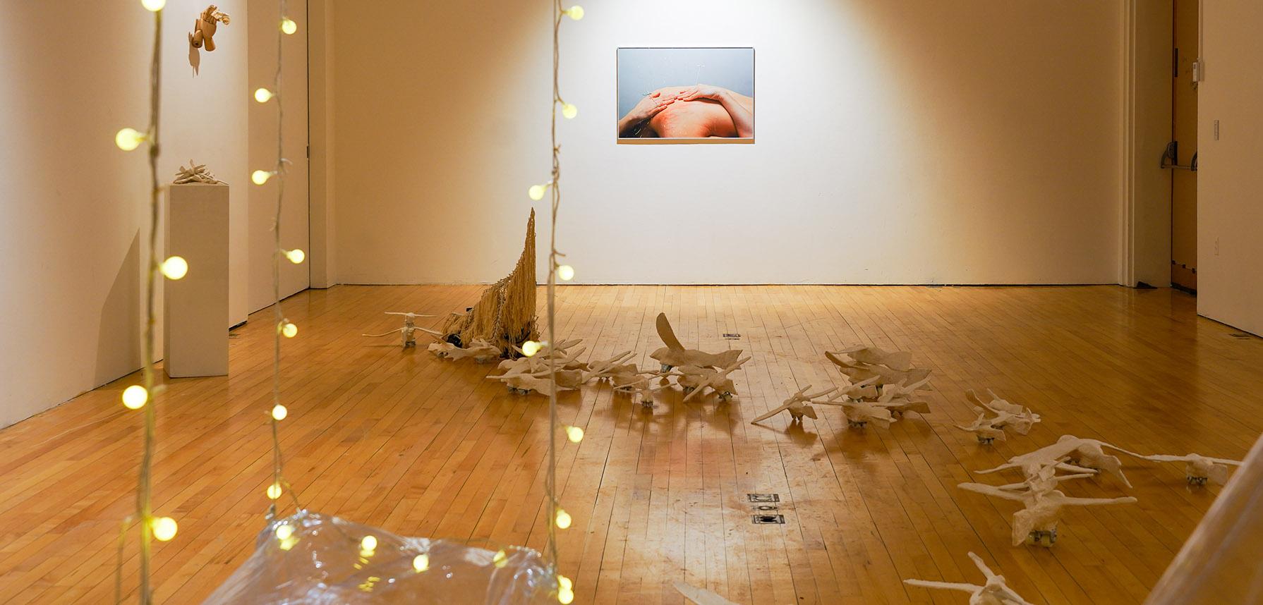 Airplane and bone sculptures on a wooden floor with hanging lights and a photo on a wall.