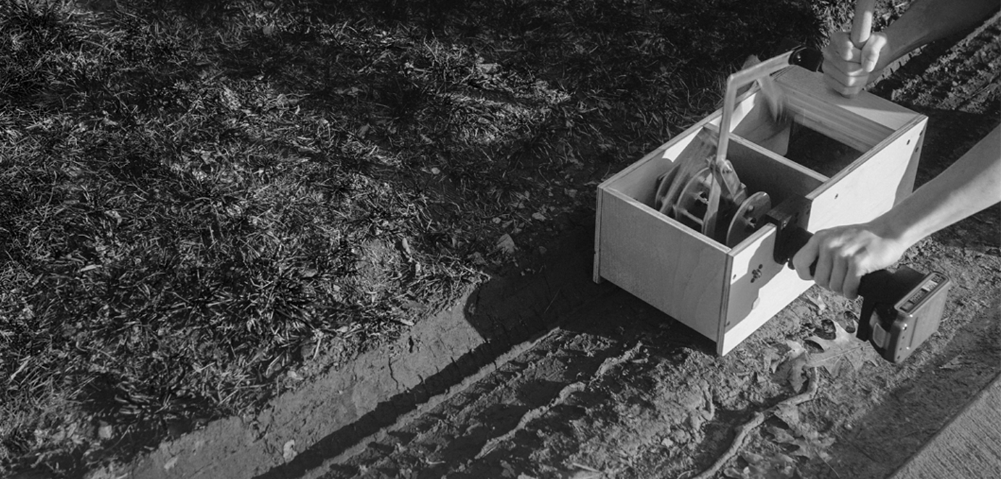 Drill-powered hand-tool encased in wooden box, operated by person out of view.