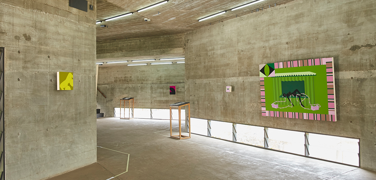 Multiple square and rectangular paintings hang in a concrete gallery with lights lining the hallway of the gallery along the bottom of the walls.