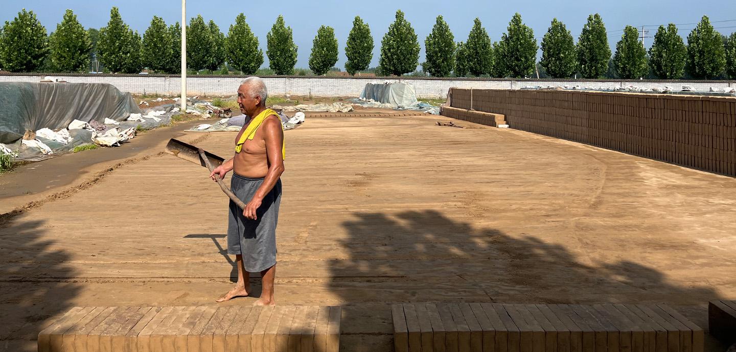 Person standing in an open lot that is edged by clay bricks.