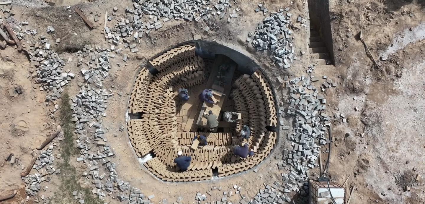 Aerial image of a kiln fully loaded with bricks in a circular fashion, with five people inside the kiln stacking bricks.