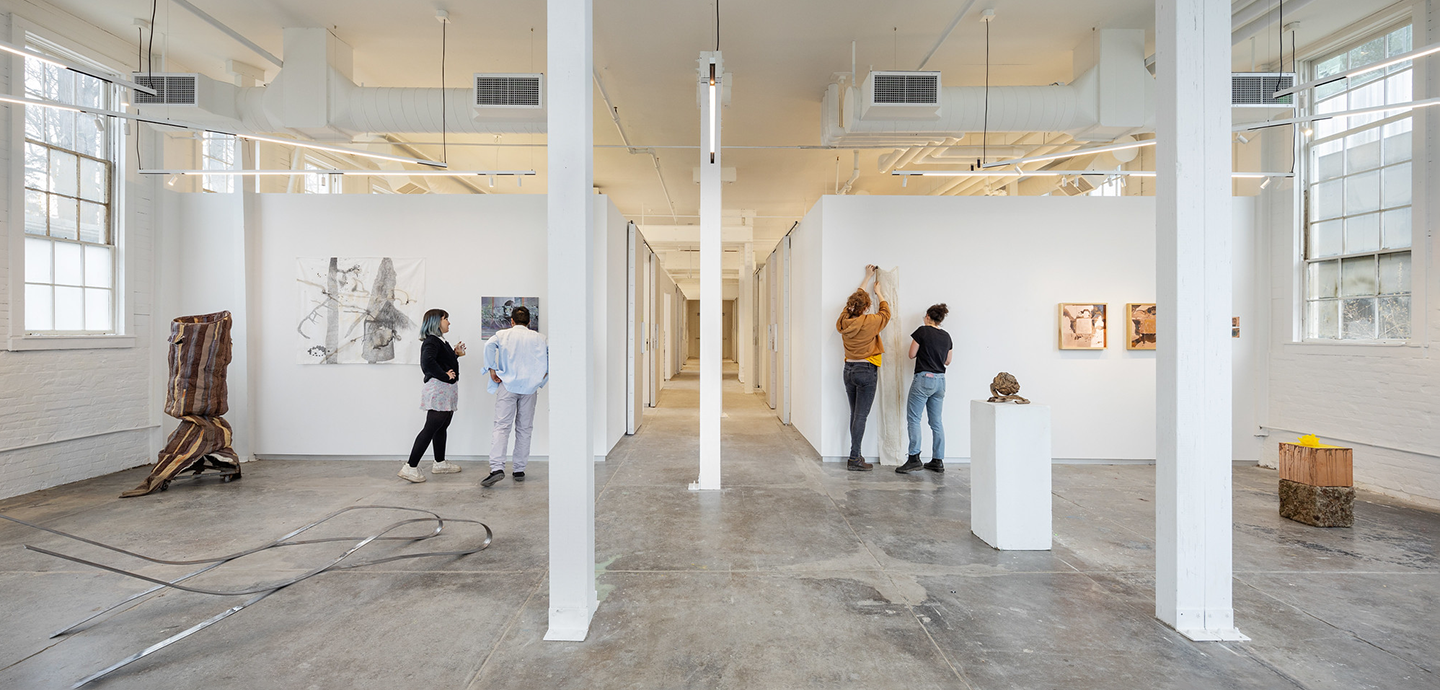 Four people standing in a large open gallery painted white.