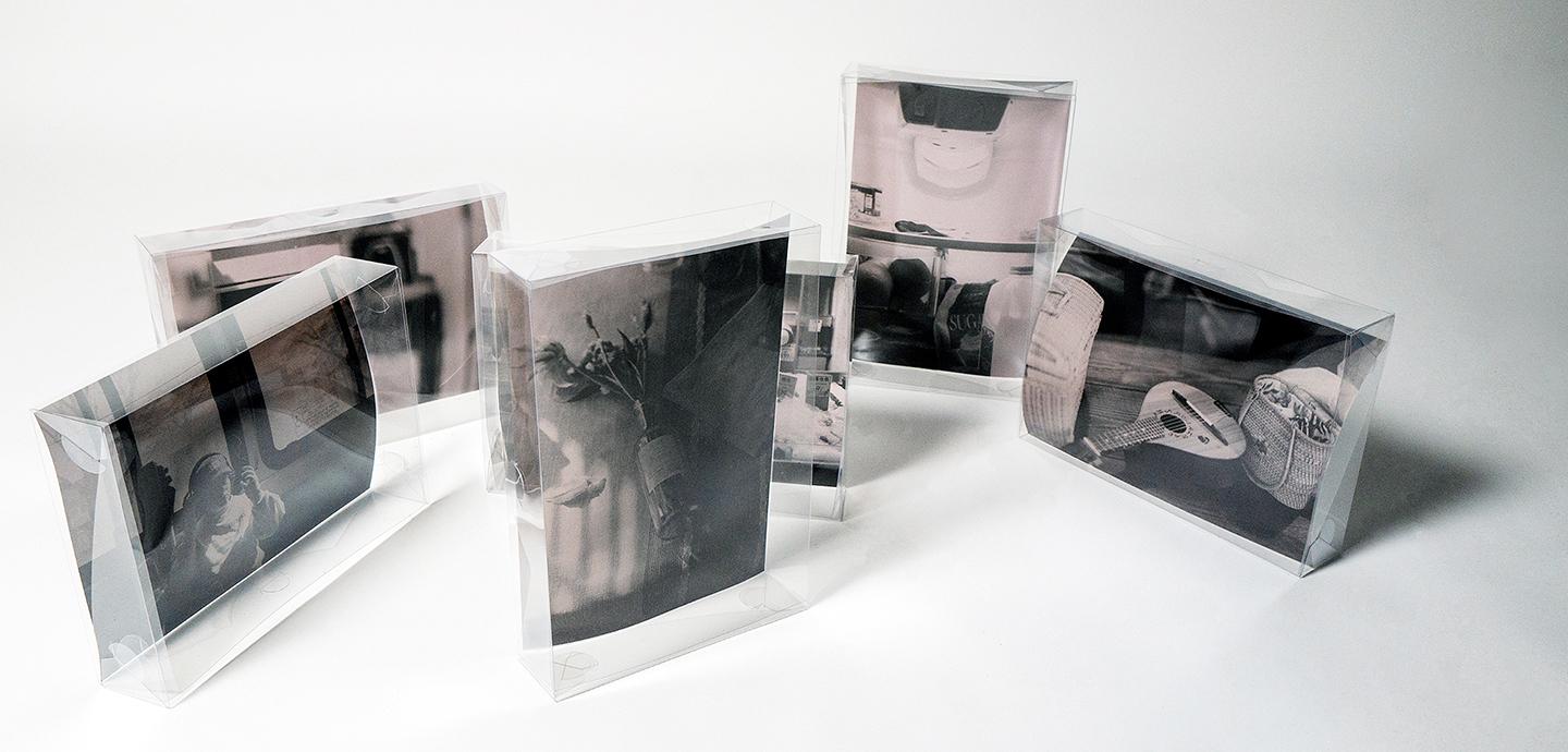 A set of five black-and-white still life photographs in clear display cases.