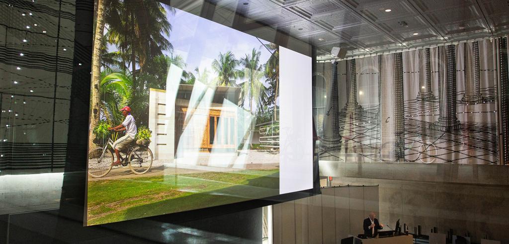 A large screen in an auditorium with an image of a person riding their bike next to a building.