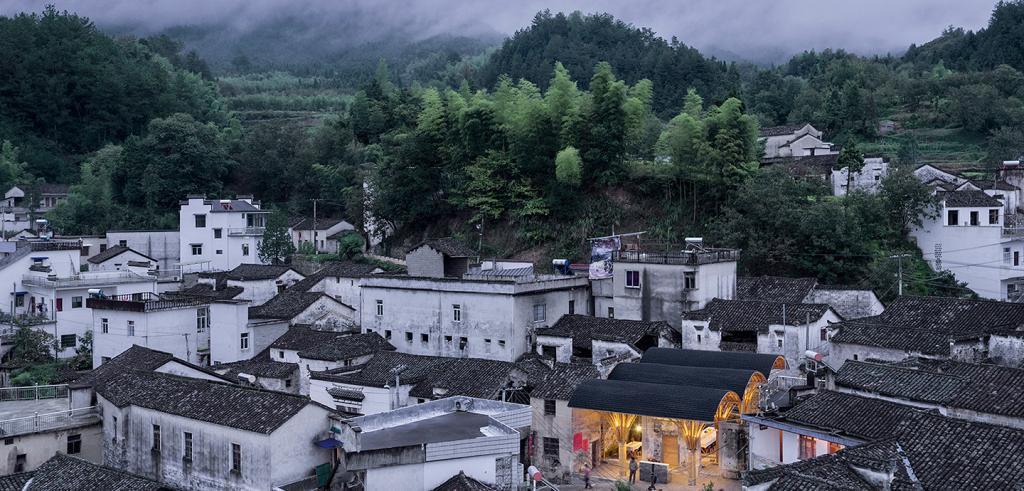 White buildings with grey and black roof tiles surrounded by trees and low hanging clouds.