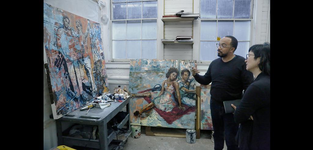 Two people looking at a painting propped on a wall in a person's studio.