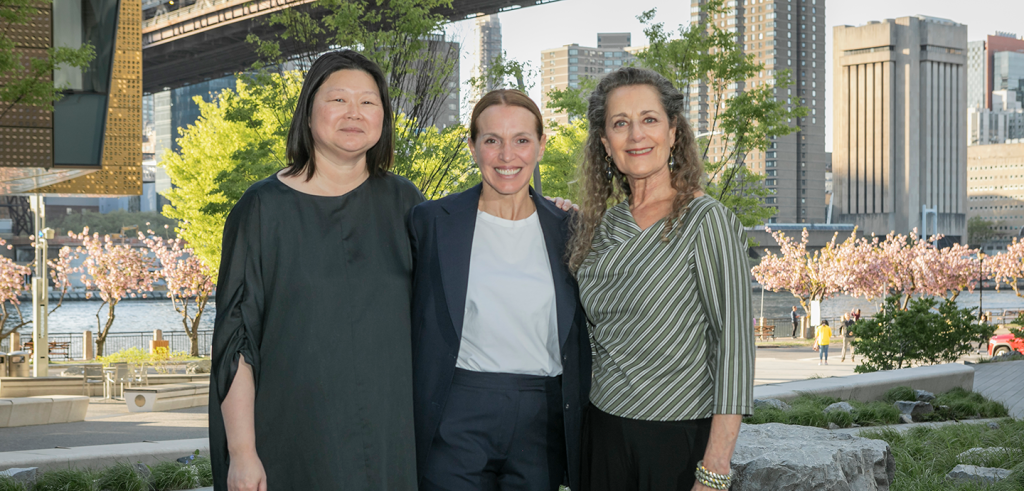 three people standing next to each other with large buildings behind them