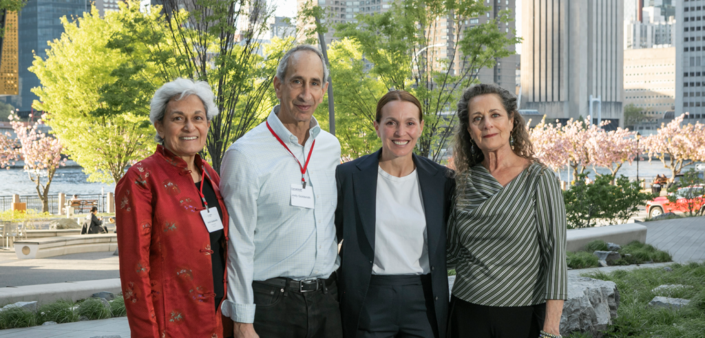 four people standing next to each other with large buildings behind them