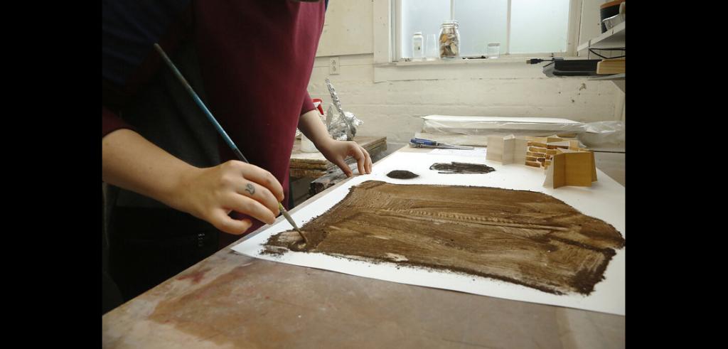 Close up of a person painting a brown image on white paper.