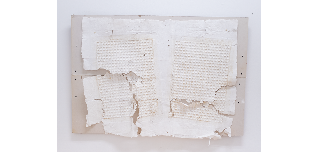 Handmade paper embossed with a circular grid pattern, torn in some places, nailed with screws to a piece of drywall.