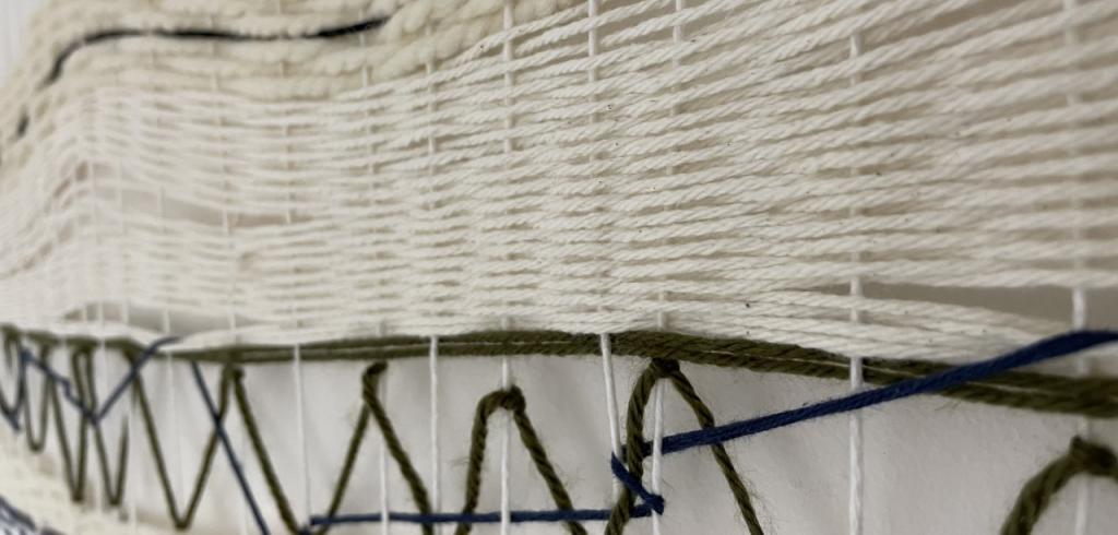 White yarn tapestry with stripes of dark brown and one dark blue piece.