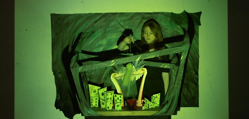 Green video still of a woman with long hair working on a cartoon depiction of abstract dominos.