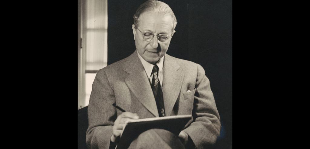 Man seated in a dark chair, wearing a light suit