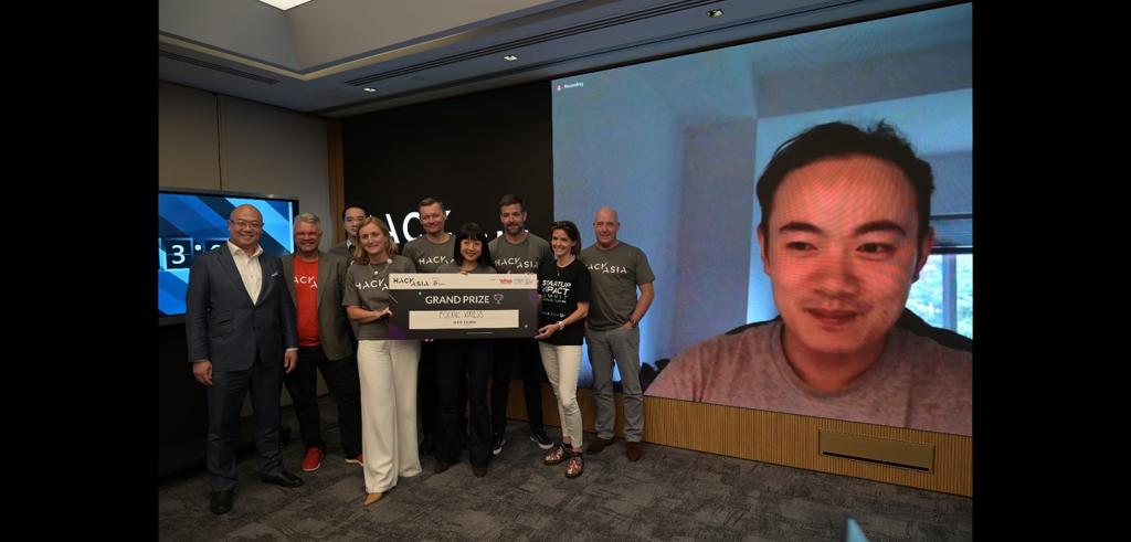 A group of people holding a sign beside a large LCD screen picturing a man's face