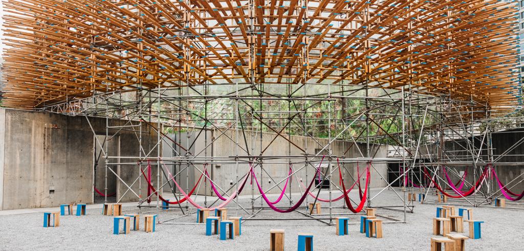 Large cyclorama which features a panoramic image of the jungle on scaffolding, with pink hammocks suspended beneath. 