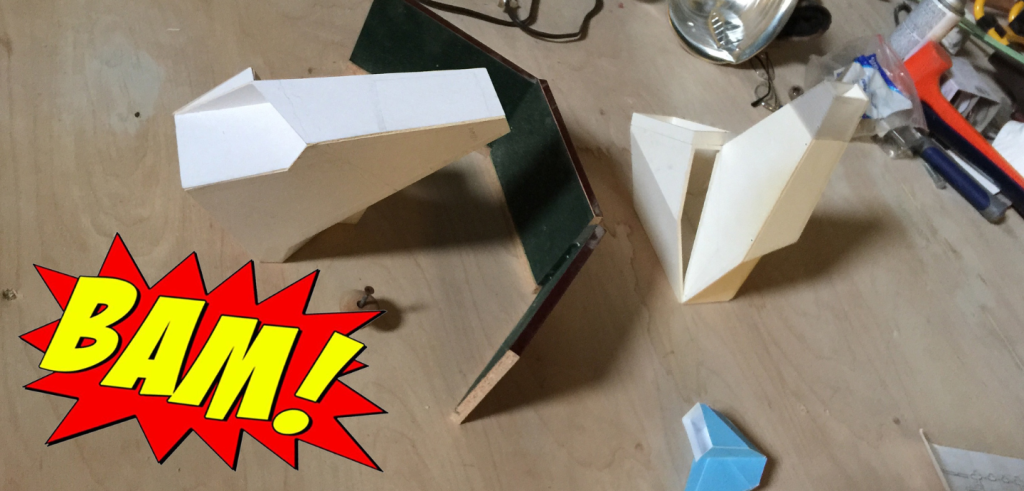 A desk scattered with items including deliberately folded paper. A yellow and red graphic saying BAM! is in the lower left corner