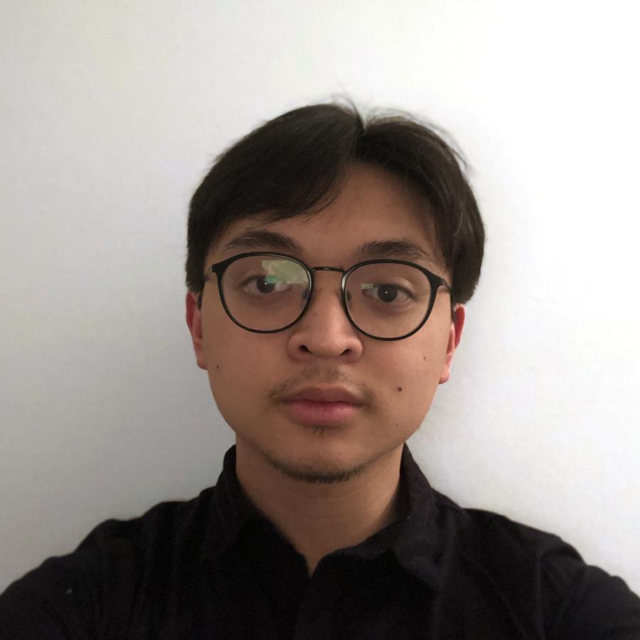 A headshot of a man with dark parted black hair and glasses against a white wall.